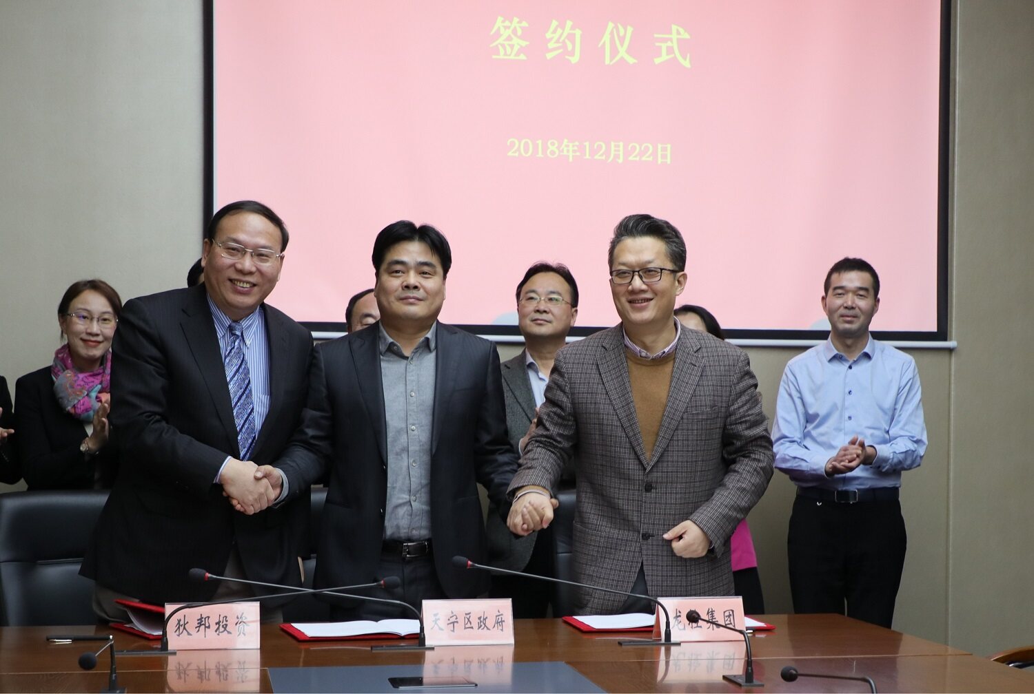 A group of men shake hands in front a presentation in Chinese