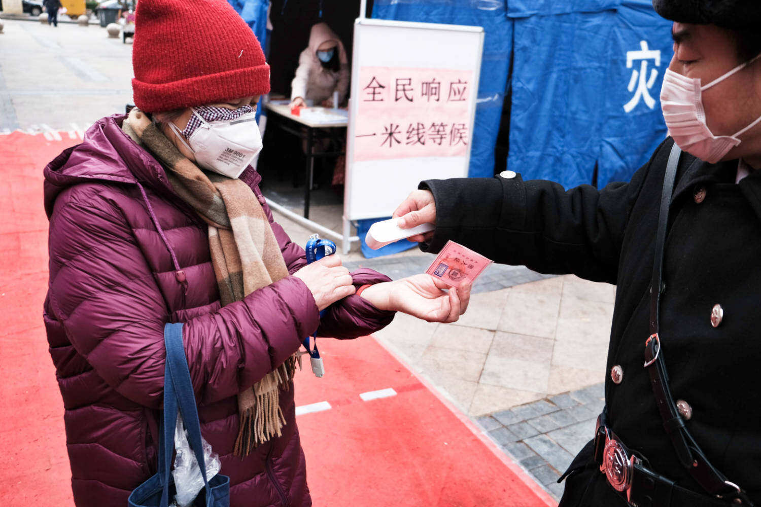 A guard performs a coronavirus health check on an elderly woman